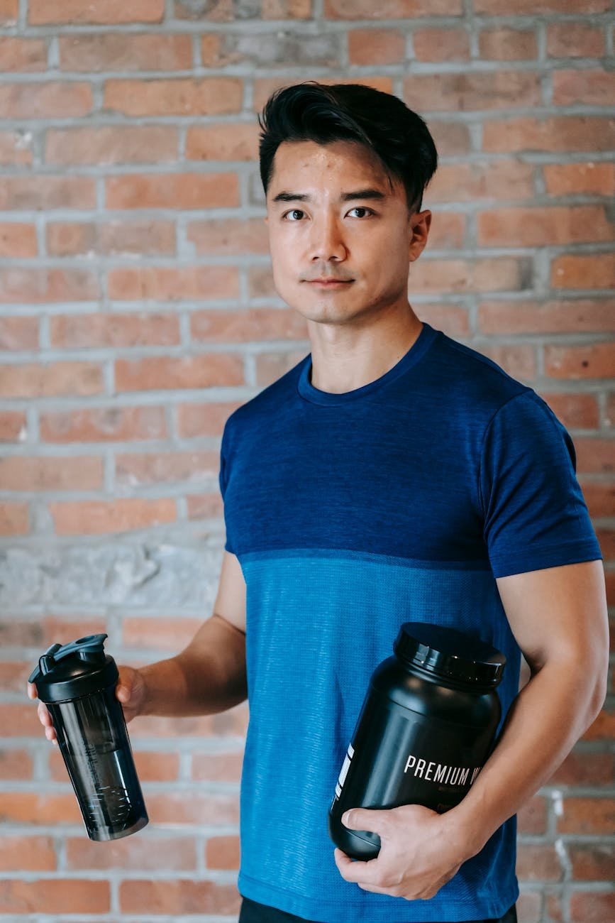 ethnic sportsman standing with protein jar and water bottle